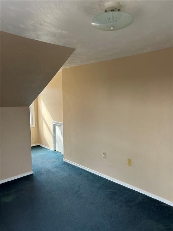 additional living space with baseboards and dark colored carpet