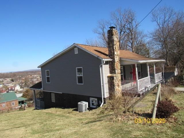 view of home's exterior featuring covered porch, cooling unit, a chimney, and a yard