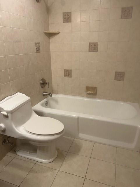 bathroom featuring tile patterned flooring, toilet, bathing tub / shower combination, and tile walls