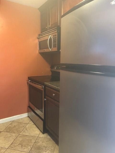 kitchen featuring dark countertops, light tile patterned floors, stainless steel appliances, and baseboards