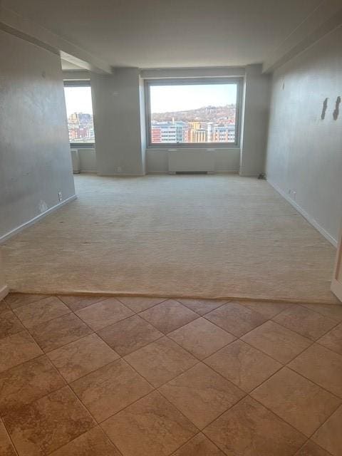 carpeted empty room featuring a wealth of natural light, baseboards, and tile patterned floors