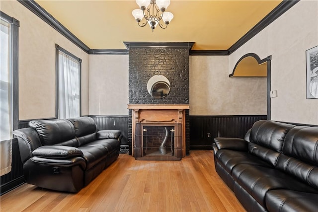 living room featuring a wainscoted wall, a fireplace, wood-type flooring, crown molding, and a notable chandelier