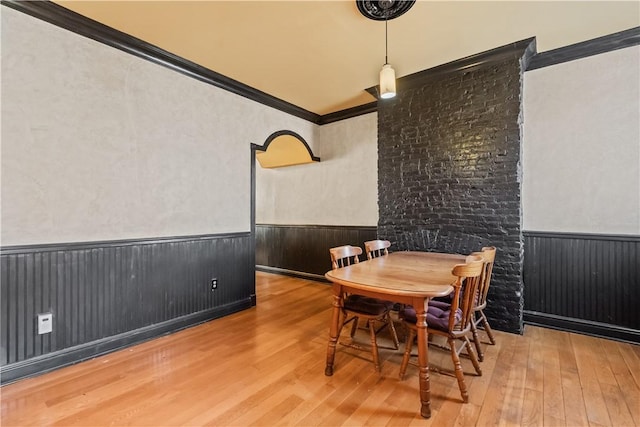 dining space featuring wood-type flooring, wainscoting, and crown molding