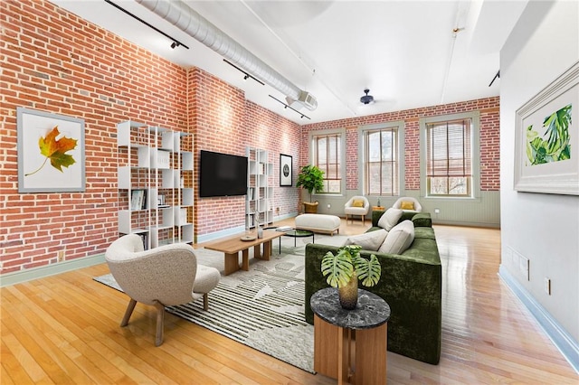 living area with hardwood / wood-style flooring, brick wall, and track lighting