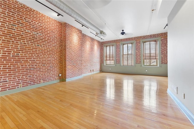 unfurnished room with track lighting, wood-type flooring, baseboards, and brick wall