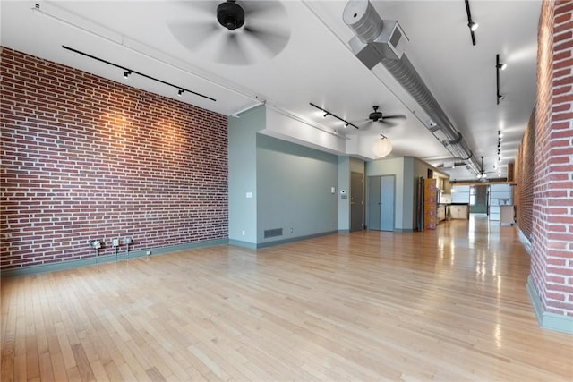 unfurnished room featuring track lighting, wood finished floors, brick wall, and ceiling fan