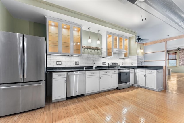 kitchen featuring dark countertops, light wood finished floors, tasteful backsplash, stainless steel appliances, and a sink