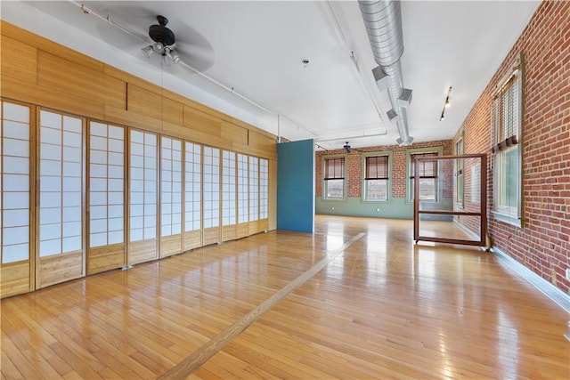 spare room featuring track lighting, brick wall, a ceiling fan, and hardwood / wood-style floors