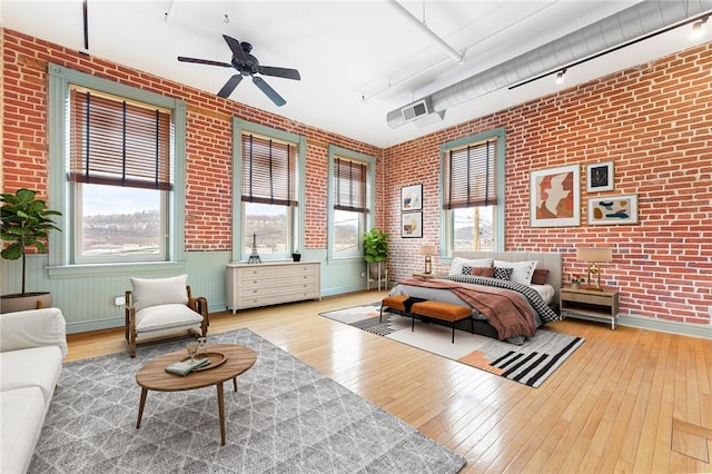 bedroom with track lighting, brick wall, baseboards, and hardwood / wood-style flooring