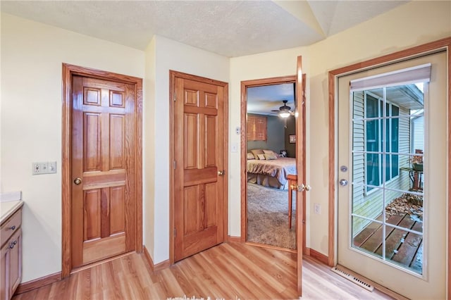 hallway featuring visible vents, baseboards, a textured ceiling, and light wood finished floors