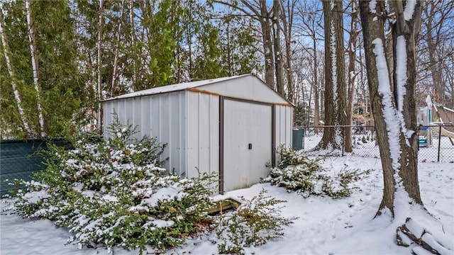 snow covered structure with a storage shed, fence, and an outbuilding