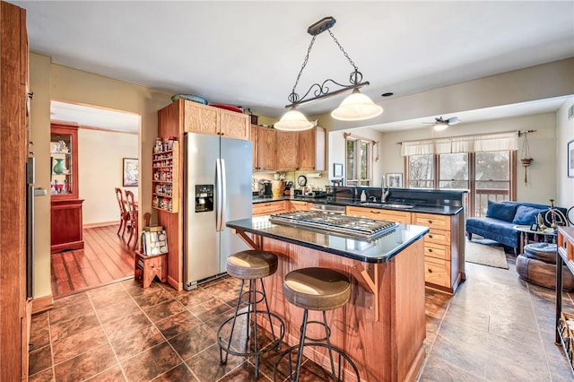 kitchen featuring a breakfast bar, a sink, dark countertops, appliances with stainless steel finishes, and a peninsula