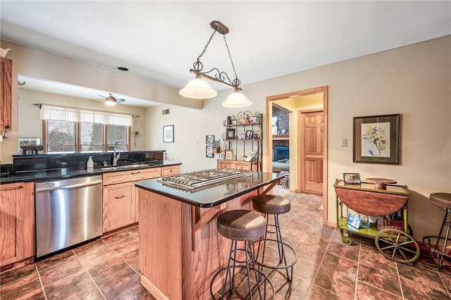 kitchen with a kitchen bar, a sink, dark countertops, a center island, and appliances with stainless steel finishes