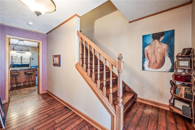 stairs featuring baseboards, wood-type flooring, visible vents, and crown molding