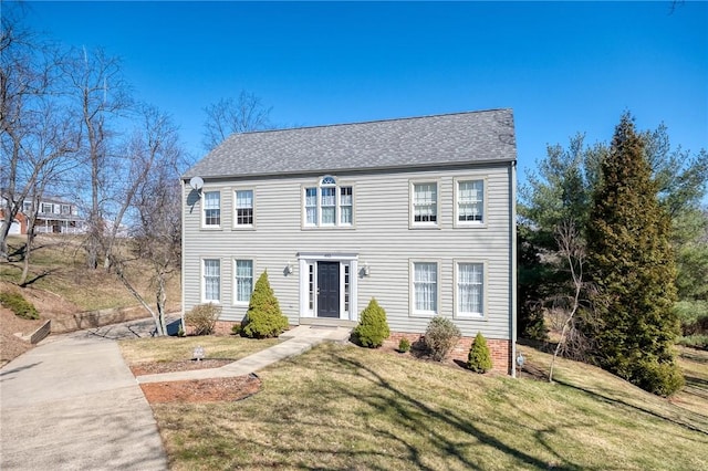 colonial house featuring a front lawn and roof with shingles