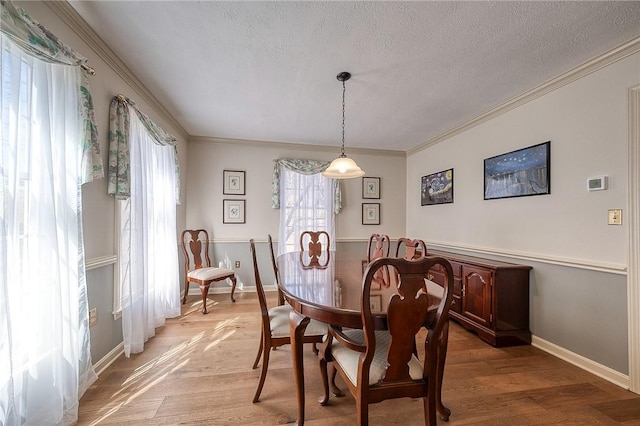 dining room featuring ornamental molding, light wood-style floors, baseboards, and a textured ceiling