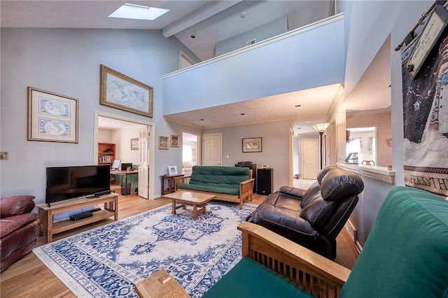 living area featuring beam ceiling, high vaulted ceiling, a skylight, and light wood-type flooring