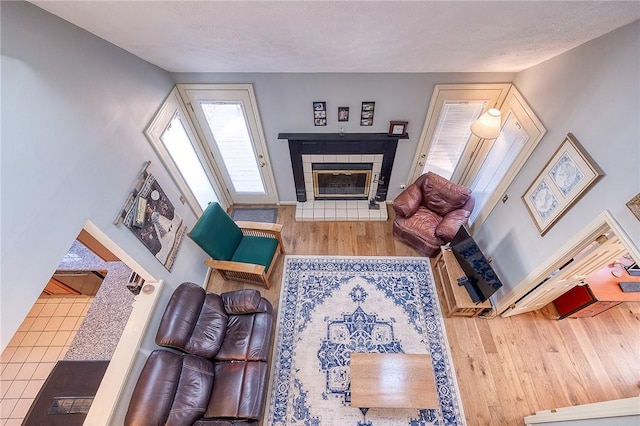 living room featuring a tile fireplace, a textured ceiling, baseboards, and wood finished floors