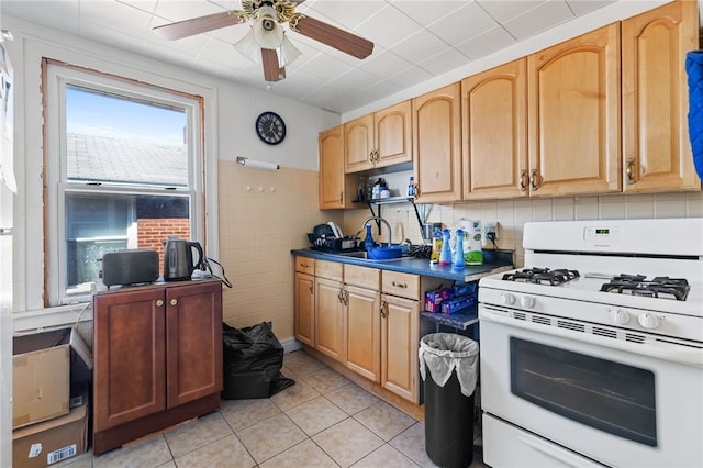 kitchen with dark countertops, tile walls, light tile patterned flooring, white range with gas stovetop, and ceiling fan