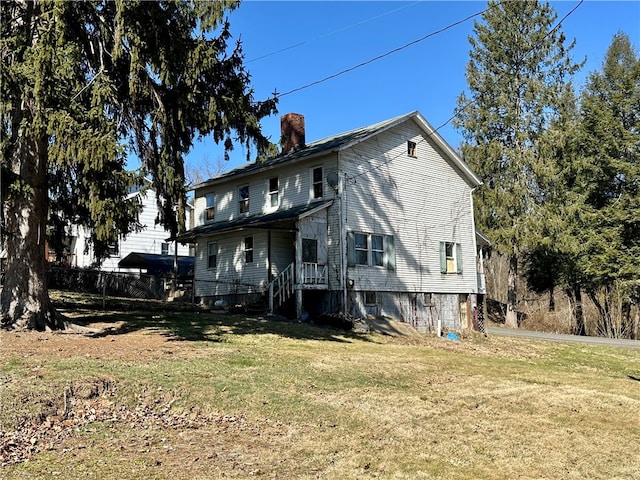 rear view of house featuring a chimney, a yard, and fence