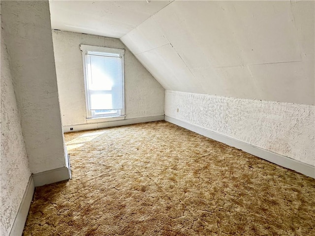 additional living space featuring a textured wall, lofted ceiling, and carpet floors