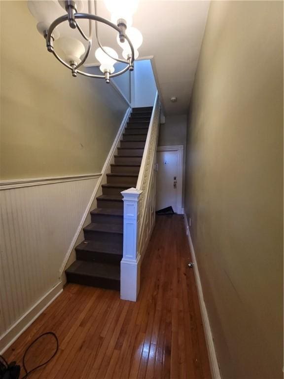 stairway with a wainscoted wall, wood-type flooring, and an inviting chandelier