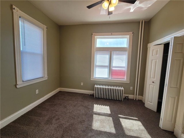 unfurnished bedroom with dark colored carpet, baseboards, radiator, and a ceiling fan