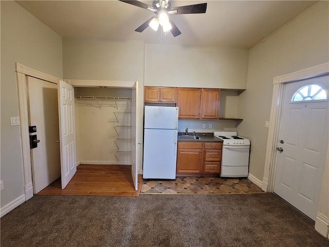 kitchen featuring dark countertops, dark carpet, brown cabinets, white appliances, and a sink