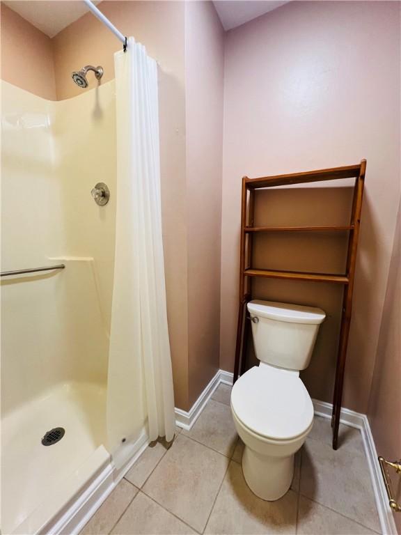 full bath featuring tile patterned flooring, a shower stall, toilet, and baseboards