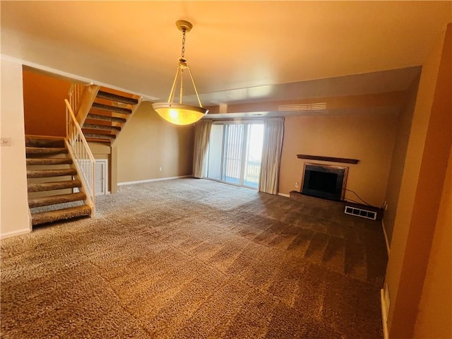 unfurnished living room with visible vents, a fireplace with raised hearth, carpet flooring, baseboards, and stairs