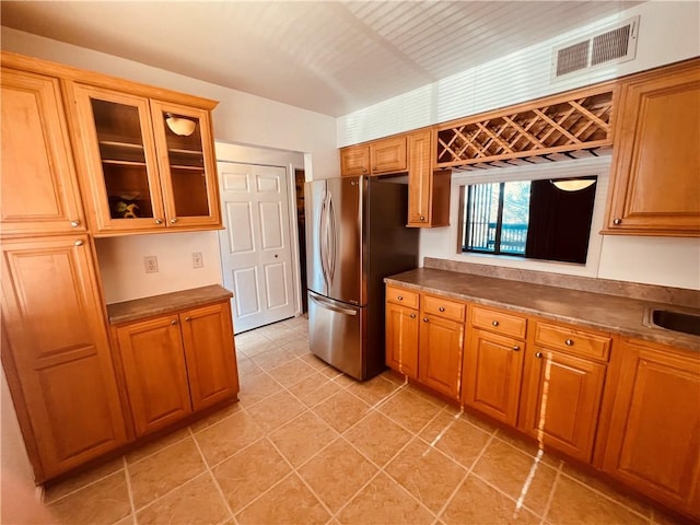 kitchen with brown cabinetry, glass insert cabinets, visible vents, and freestanding refrigerator