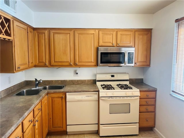 kitchen featuring brown cabinetry, a healthy amount of sunlight, white appliances, and a sink