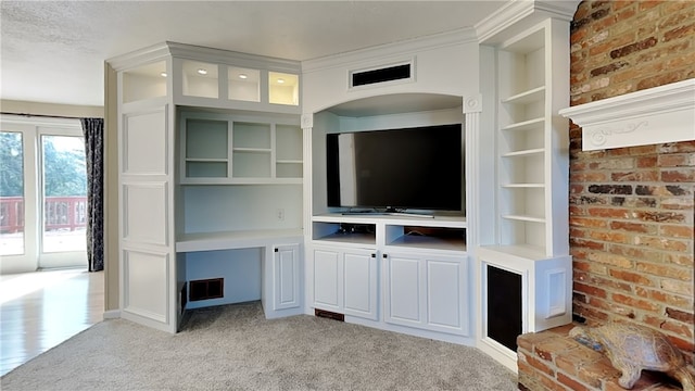 unfurnished living room featuring built in shelves, light colored carpet, ornamental molding, and brick wall