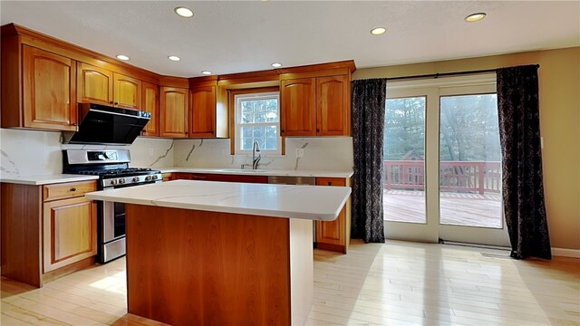 kitchen with stainless steel gas stove, light wood-style flooring, a sink, a kitchen island, and recessed lighting