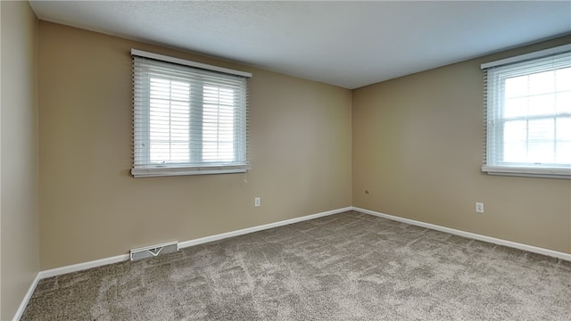 carpeted empty room featuring plenty of natural light, baseboards, and visible vents