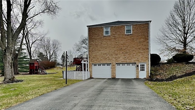 view of property exterior featuring a lawn, aphalt driveway, a playground, a garage, and brick siding