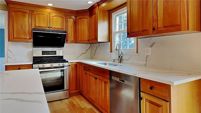 kitchen with light wood-type flooring, a sink, tasteful backsplash, stainless steel appliances, and light stone countertops