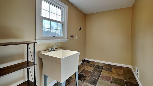 washroom with a sink, visible vents, baseboards, and stone tile floors