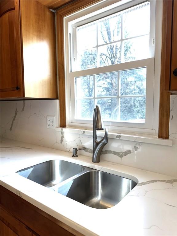 room details with a sink, decorative backsplash, light stone counters, and brown cabinetry