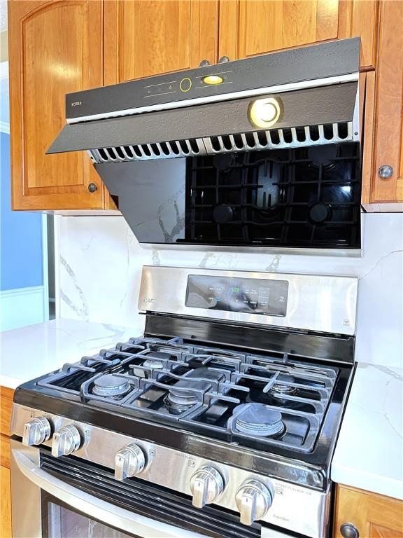 room details featuring brown cabinetry, decorative backsplash, gas range, and light countertops