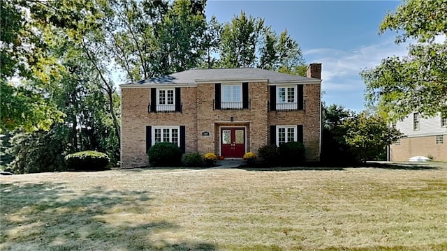 colonial home featuring french doors, brick siding, a chimney, and a front lawn