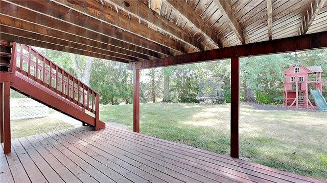 wooden terrace featuring a playground, stairs, a trampoline, and a lawn