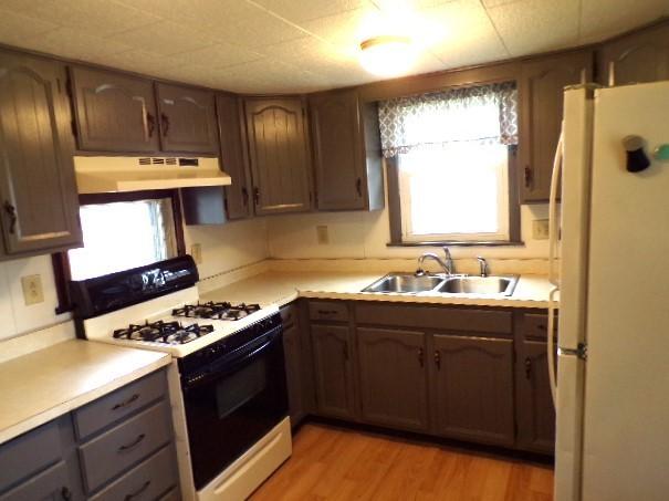 kitchen with light wood-type flooring, under cabinet range hood, a sink, range with gas stovetop, and freestanding refrigerator