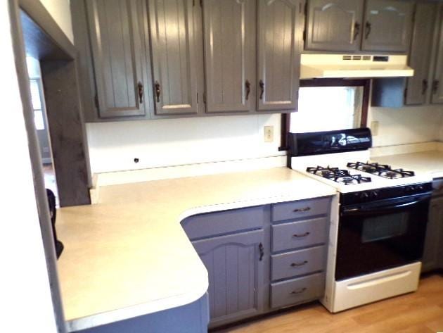 kitchen with gray cabinetry, under cabinet range hood, light countertops, light wood-style floors, and gas stove