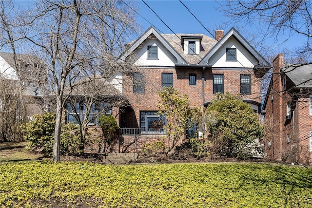 tudor home with a front lawn, brick siding, and a chimney