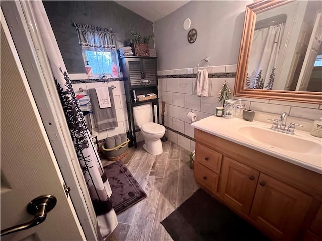 bathroom featuring toilet, wood finished floors, tile walls, wainscoting, and vanity