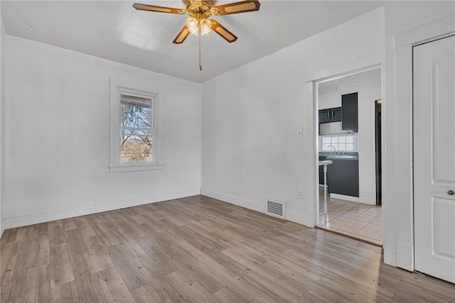 unfurnished room featuring a ceiling fan, wood finished floors, baseboards, and a sink