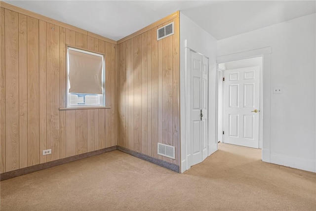 carpeted spare room with baseboards, visible vents, and wood walls