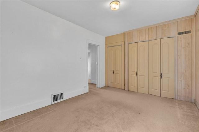 unfurnished bedroom with baseboards, visible vents, two closets, and carpet