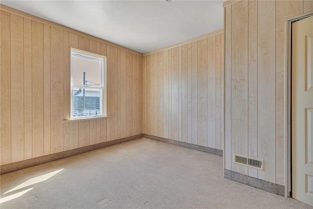 unfurnished room with visible vents, baseboards, wood walls, and carpet flooring